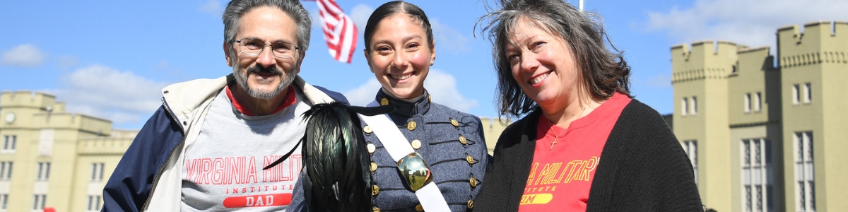 Female cadet poses for a photo with her parents who are wearing ϲ shirts.