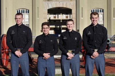 Four cadets who received direct commissions into the U.S. Coast Guard through ϲ, a military college, pose in front of barracks.